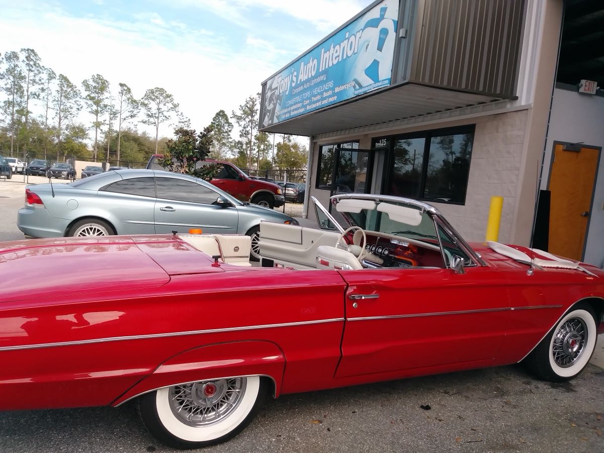 A restored red classic convertible parked in front of the Tony's Auto Interior storefront in Orlando